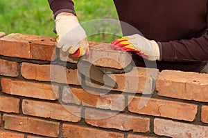 A man builds a wall of bricks, lays a brick on a cement-sand mortar