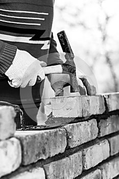 A man builds a wall of bricks, lays a brick on a cement-sand mortar, tapping a brick with a hammer