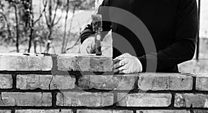 A man builds a wall of bricks, lays a brick on a cement-sand mortar, tapping a brick with a hammer