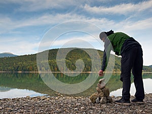 Man built pyramid from pebbles. Balanced stone pyramide on shore of blue water of mountain lake.