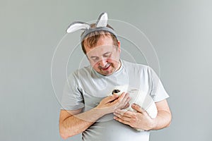 A man with bunny ears and a gray T-shirt is holding a white rabbit.