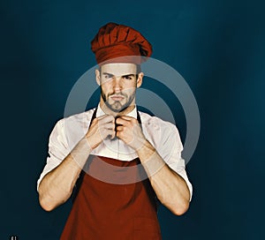 Man in burgundy cook hat and apron. Cook works in kitchen. Cuisine and professional cooking concept