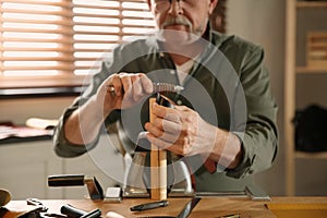 Man burnishing edges of leather belt in workshop photo
