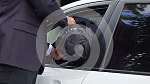 Man in business suit giving bag with money or weapon to man in car, criminality