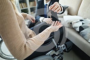 Man in business suit giving keys to apartment to disabled woman in wheelchair closeup