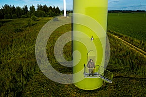 A man in a business suit with a green Golf shirt stands next to a windmill against the background of the field and the blue sky.