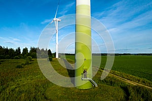 A man in a business suit with a green Golf shirt stands next to a windmill against the background of the field and the blue sky.