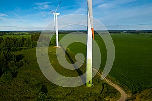 A man in a business suit with a green Golf shirt stands next to a windmill against the background of the field and the blue sky.