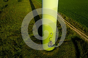 A man in a business suit with a green Golf shirt stands next to a windmill against the background of the field and the blue sky.