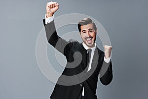 Man business in a suit happy smile with teeth raised hands up clenched fists on a gray background. The joy of winning in