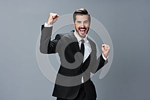 Man business in a suit happy smile with teeth raised hands up clenched fists on a gray background. The joy of winning in