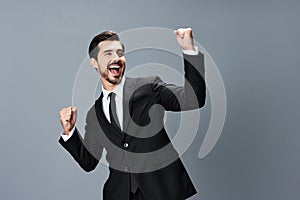 Man business in a suit happy smile with teeth raised hands up clenched fists on a gray background. The joy of winning in