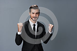 Man business in a suit happy smile with teeth raised hands up clenched fists on a gray background. The joy of winning in