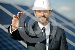 Man in business suit holding photovoltaic detail of solar panel.