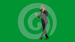 Man in business suit with horse head mask on green studio background. Businessman walking and talking on smartphone