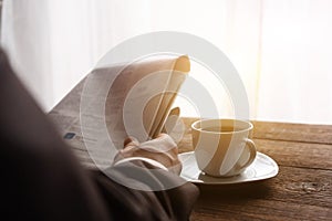 A man in a business suit in the morning in the sun reads the news in the newspaper, next to a cup of black coffee. Reading