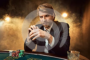 A man in a business suit sitting at the game table. Male player. Passion, cards, chips, alcohol, dice, gambling, casino