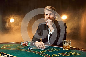 A man in a business suit sitting at the game table. Male player. Passion, cards, chips, alcohol, dice, gambling, casino