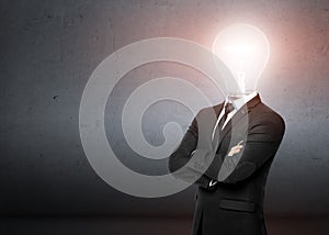 Man in a business suit stands, behind him empty concrete wall. Instead of head businessman lighting bulb. Bussines, idea