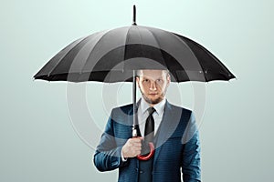 A man in a business suit stands with an umbrella in his hands on a light background. Savings and assets protection, insurance