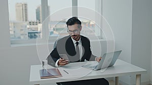 Man in business suit wearing glasses tardy working in office laptop and phone on desk at workplace, online working at