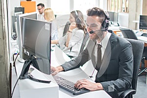 Man in business wear with headset working on desktop computer in customer service call support helpline business center