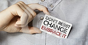 A man businessman in a blue shirt holds a card in a pocket with the text Do Not Resist Change Embrace It in his hand