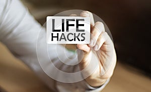 A man businessman in a blue shirt holds a card with the text Life Hacks in his hand