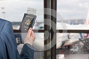 Man businessman  in a blue suit  holding american passport with boarding pass in the airport waiting zone looking through the
