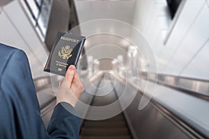 Man businessman in a blue suit with suitcase holding american passport with boarding pass on the airport escalator.