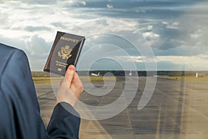 Man businessman  in a blue suit with suitcase holding american passport with boarding pass in the airport waiting zone looking