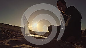 Man businessman freelancer talking on the phone working behind laptop sitting on beach freelancing silhouette in the sun