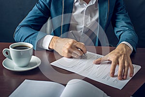 Businessman signs important legal documents on the desktop with Cup of coffee