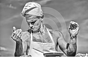Man on busy face wears cooking hat and apron, sky on background. Cook or chef with sexy muscular shoulders and chest