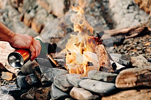 Man with a butane can burner kindles a fire in a bonfire on a stone beach