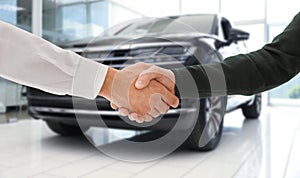 Man buying car and shaking hands with salesman against blurred auto