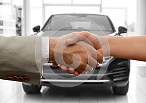 Man buying car and shaking hands with salesman against blurred auto