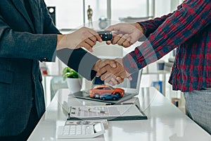 Man buys car and shakes hands with business salesman, closing car sales agreement, gesture and concept of giving keys to new owner