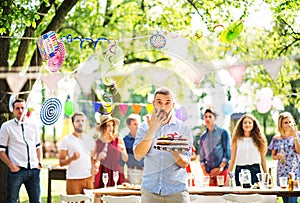 Man with a cake on a family celebration or a garden party outside, licking his finger.