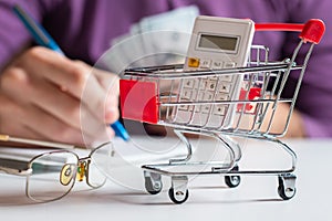 Man calculates the budget. Shopping cart a on table with calculator and paper