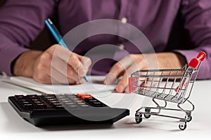 Man calculates the budget. Shopping cart a on table with calculator and paper