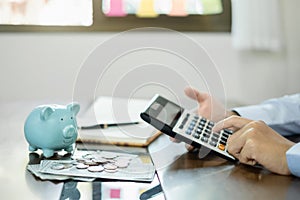 Man calculating her expenses on a notebook putting coin into piggy bank. Saving money with coins Step into a business that is