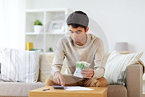 Man with calculator counting money at home