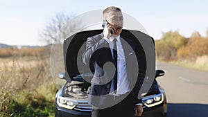 Man calling car assistance services. Unhappy businessman speak on phone near the broken electric car help repair stress