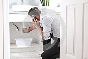 Man Calling Plumber In Front Of Water Leaking From Sink Pipe