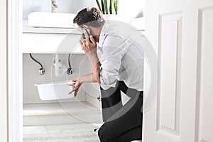 Man Calling Plumber In Front Of Water Leaking From Sink Pipe