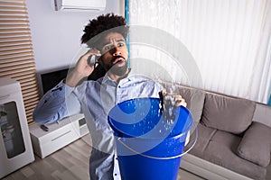 Man Calling Plumber While Leakage Water Falling Into Bucket