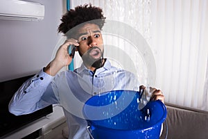 Man Calling Plumber While Leakage Water Falling Into Bucket