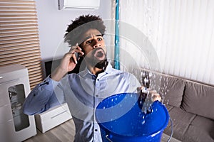 Man Calling Plumber While Leakage Water Falling Into Bucket