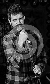 Man with calm face holds microphone, singing song, black background. Guy likes to sing rock songs. Musician with beard